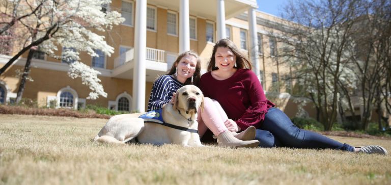 Two females in front of Dawson Hall with service dog